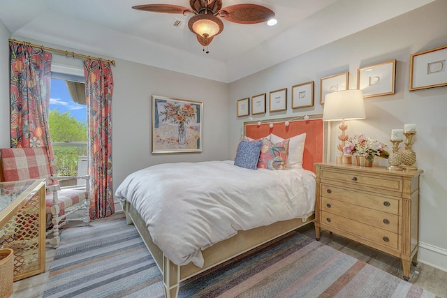 bedroom with a tray ceiling, wood finished floors, visible vents, baseboards, and ceiling fan