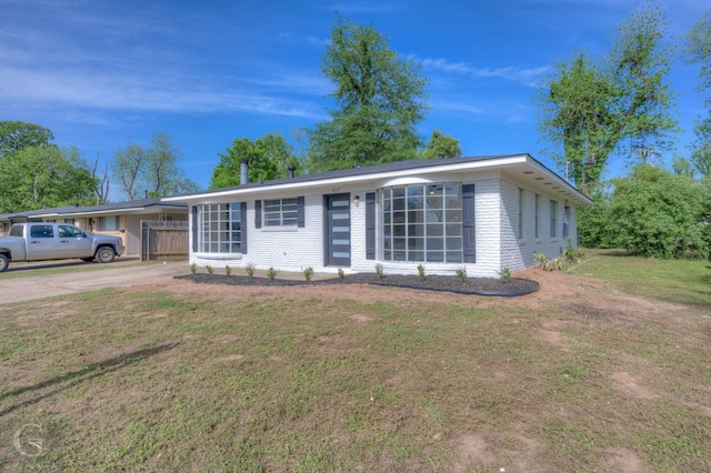 single story home featuring brick siding, driveway, a front yard, and fence