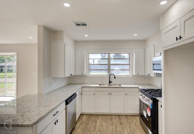kitchen featuring light stone counters, dishwasher, visible vents, a sink, and gas stove
