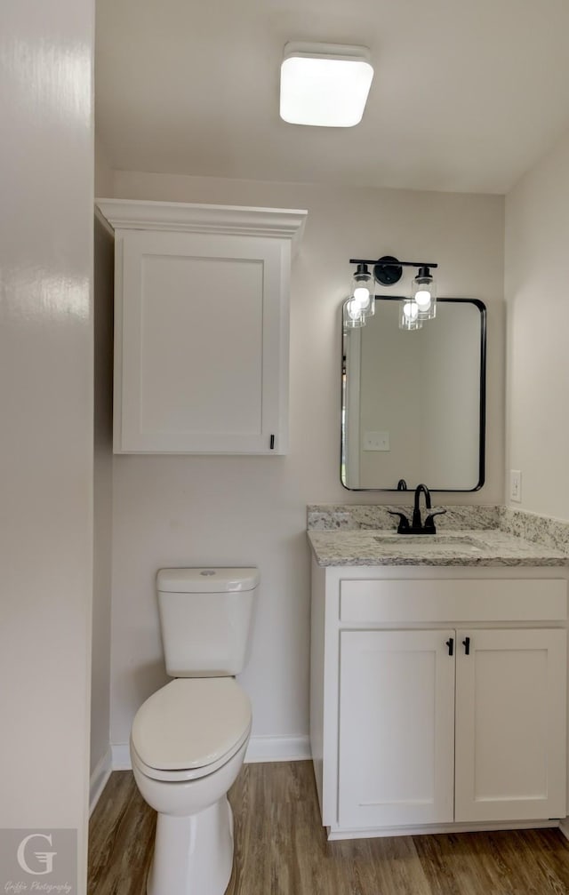 half bath featuring baseboards, vanity, and wood finished floors