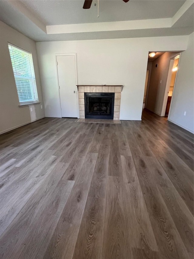 unfurnished living room featuring a tray ceiling, baseboards, a ceiling fan, wood finished floors, and a fireplace