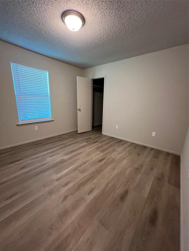 unfurnished bedroom featuring a closet, wood finished floors, a textured ceiling, and baseboards