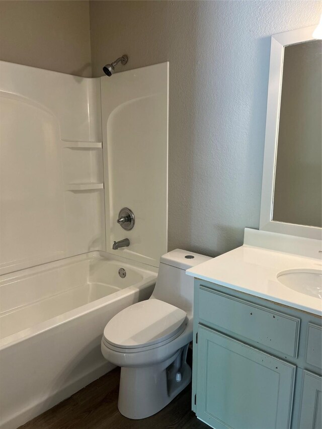 full bath featuring wood finished floors, vanity, a textured wall, shower / bath combination, and toilet