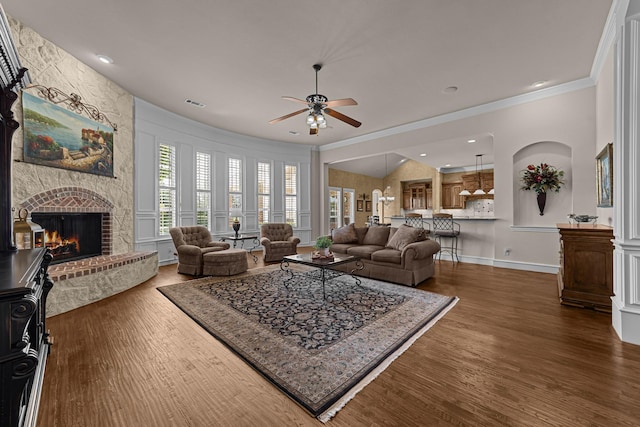 living room with crown molding, a ceiling fan, a fireplace, and dark wood-style flooring