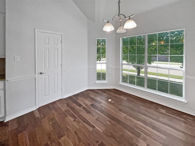 unfurnished dining area featuring high vaulted ceiling, dark wood finished floors, baseboards, and a notable chandelier