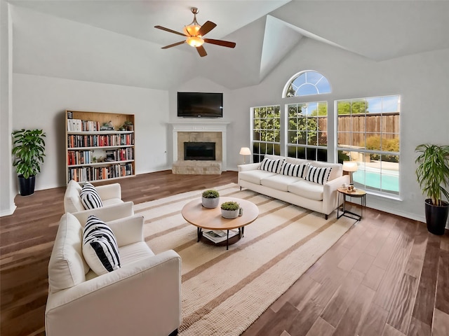 living room with vaulted ceiling, a tile fireplace, a ceiling fan, and wood finished floors