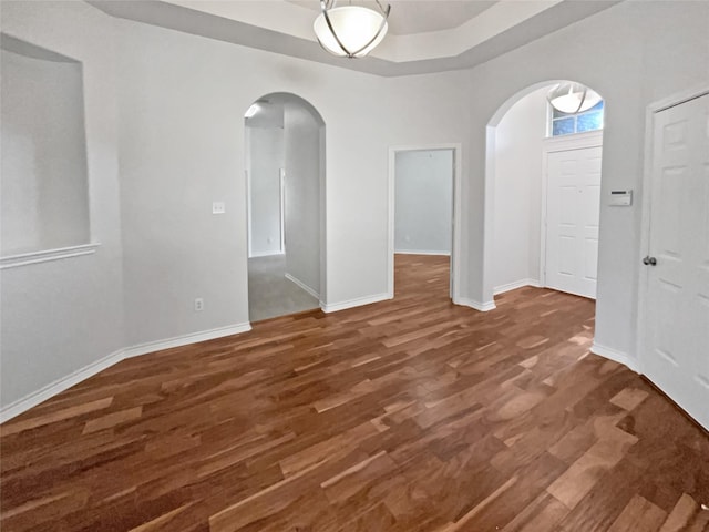 interior space featuring arched walkways, a raised ceiling, wood finished floors, and baseboards
