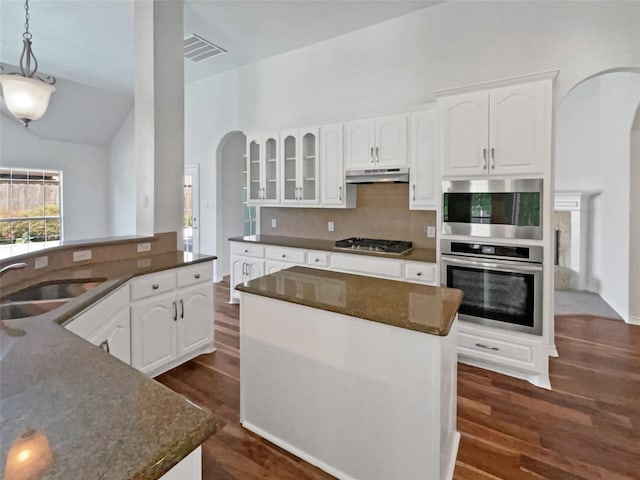 kitchen with tasteful backsplash, a sink, stainless steel gas cooktop, arched walkways, and under cabinet range hood
