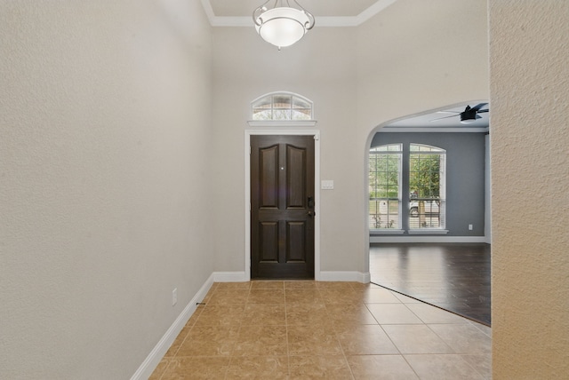 foyer entrance with a high ceiling, ornamental molding, arched walkways, light tile patterned flooring, and ceiling fan