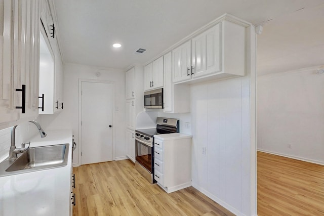 kitchen with white cabinets, a sink, baseboards, light wood-style flooring, and appliances with stainless steel finishes