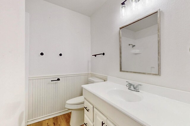 bathroom featuring wood finished floors, toilet, vanity, wainscoting, and walk in shower