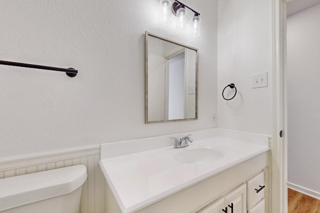 half bath with wainscoting, wood finished floors, vanity, and toilet