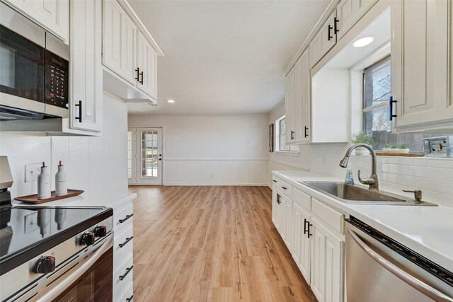 kitchen with stainless steel appliances, a sink, light wood-type flooring, decorative backsplash, and light countertops