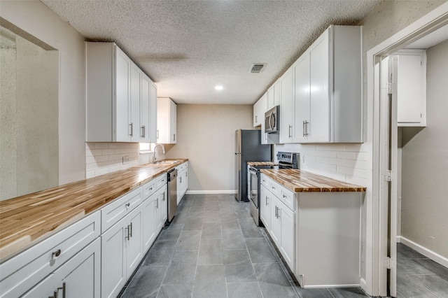 kitchen with a sink, baseboards, visible vents, butcher block countertops, and appliances with stainless steel finishes