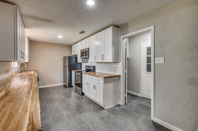 kitchen featuring stainless steel appliances, visible vents, a sink, decorative backsplash, and wood counters
