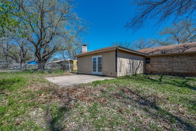rear view of house featuring fence, a chimney, french doors, and a patio