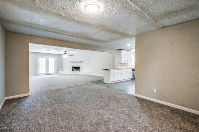 unfurnished living room featuring dark colored carpet, a fireplace with raised hearth, baseboards, and a textured wall