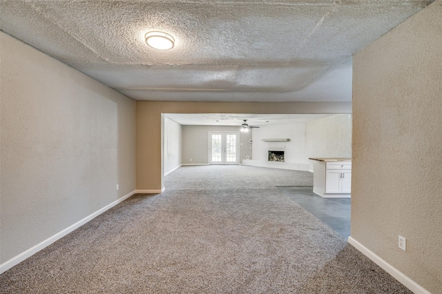 unfurnished living room featuring carpet floors, a textured wall, a fireplace with raised hearth, and baseboards