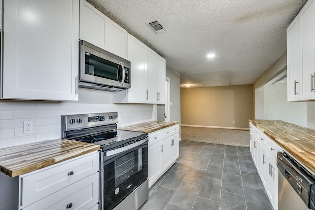 kitchen with visible vents, white cabinetry, decorative backsplash, wood counters, and appliances with stainless steel finishes