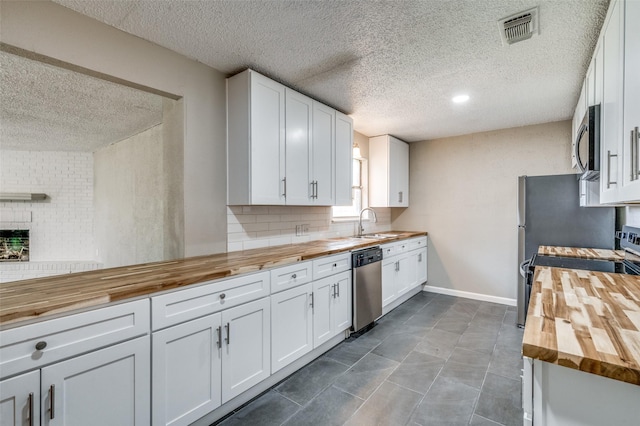 kitchen featuring butcher block countertops, a textured ceiling, white cabinets, appliances with stainless steel finishes, and visible vents