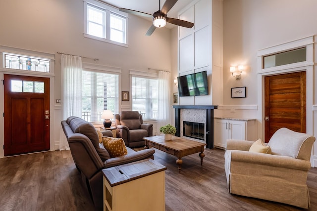living area with a ceiling fan, a towering ceiling, a fireplace, and dark wood-style flooring