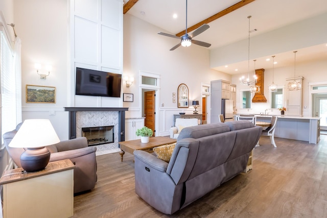 living room featuring high vaulted ceiling, wood finished floors, ceiling fan with notable chandelier, a fireplace, and beam ceiling
