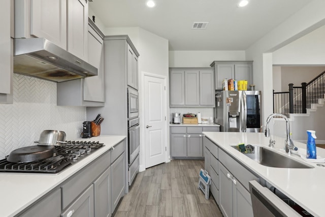 3651 Rainwater Trl, Grand Prairie, TX 76065 - kitchen featuring gray cabinetry, stainless steel appliances, a sink, exhaust hood, and tasteful backsplash