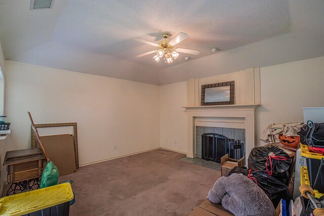 carpeted living room featuring a ceiling fan, a textured ceiling, a tiled fireplace, baseboards, and visible vents
