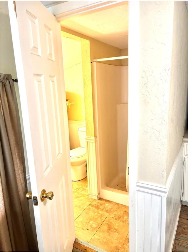 458 Jackson Ave, Strawn, TX 76475 - full bath with a shower stall, toilet, and a wainscoted wall