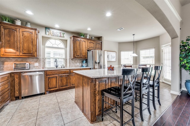 14225 Signal Hill Dr, Little Elm, TX 75068 - kitchen with stainless steel appliances, a sink, a breakfast bar area, brown cabinetry, and backsplash