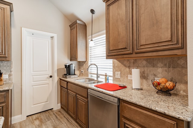 kitchen with light wood finished floors, stainless steel dishwasher, a sink, tasteful backsplash, and hanging light fixtures