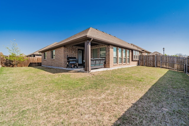 back of house featuring a fenced backyard, brick siding, a patio, and a lawn