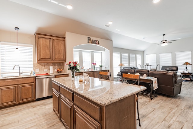 kitchen with brown cabinetry, a ceiling fan, stainless steel dishwasher, and a sink