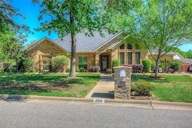 view of front of home with brick siding, roof with shingles, and a front lawn