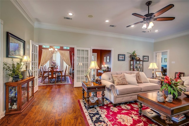 living room featuring ceiling fan with notable chandelier, visible vents, and crown molding