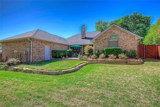 view of front of home featuring roof with shingles, a front lawn, a chimney, brick siding, and a patio