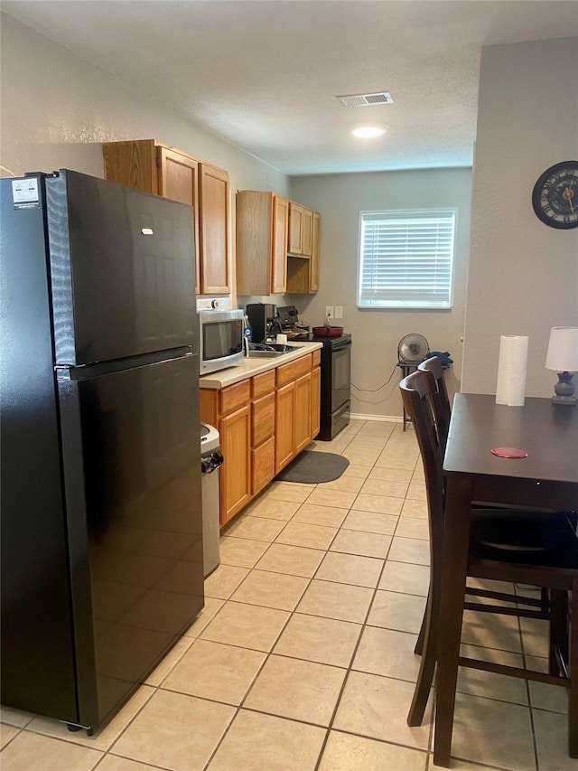 kitchen featuring black appliances, light tile patterned flooring, visible vents, and light countertops