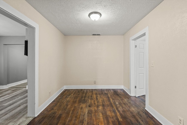 spare room featuring baseboards, wood finished floors, visible vents, and a textured ceiling