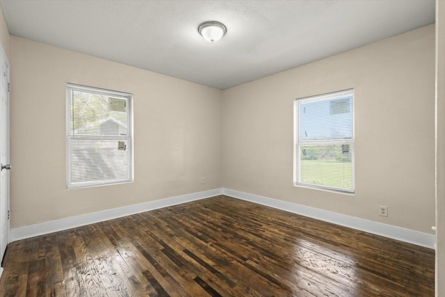 empty room featuring baseboards, dark wood-type flooring, and plenty of natural light