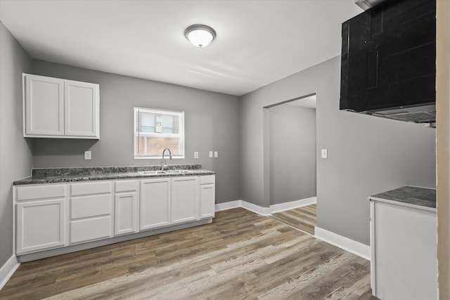 kitchen featuring white cabinets, baseboards, a sink, and light wood-style floors
