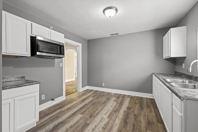 kitchen with dark wood-style floors, a sink, white cabinets, stainless steel microwave, and visible vents
