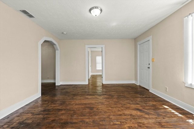 spare room with baseboards, visible vents, arched walkways, and dark wood-style flooring