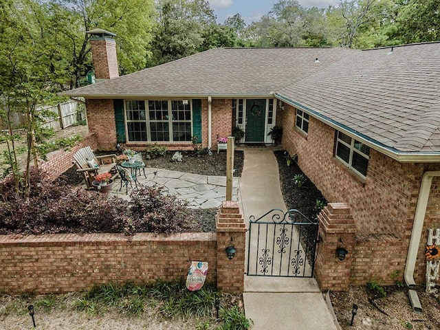 exterior space featuring a shingled roof, a chimney, brick siding, and a fenced front yard