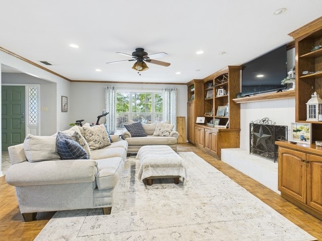 living area featuring a fireplace with raised hearth, ceiling fan, ornamental molding, visible vents, and recessed lighting