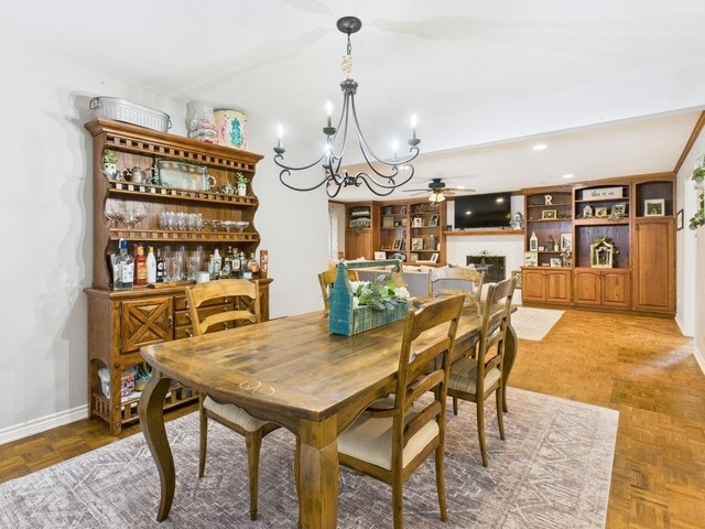 dining space with ceiling fan with notable chandelier, baseboards, and a fireplace