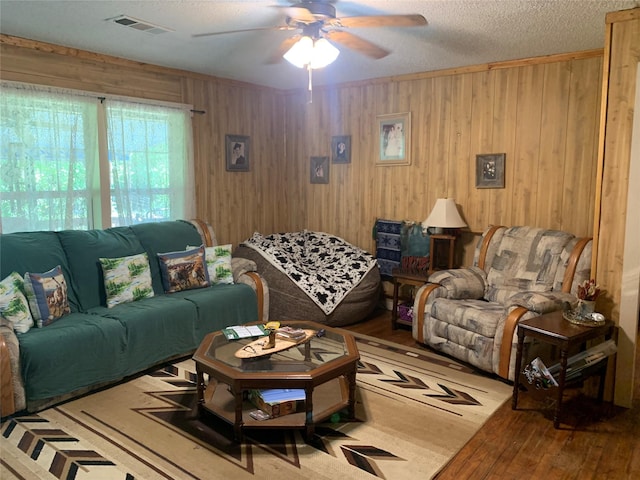 living room featuring a textured ceiling, visible vents, a ceiling fan, wood walls, and wood-type flooring