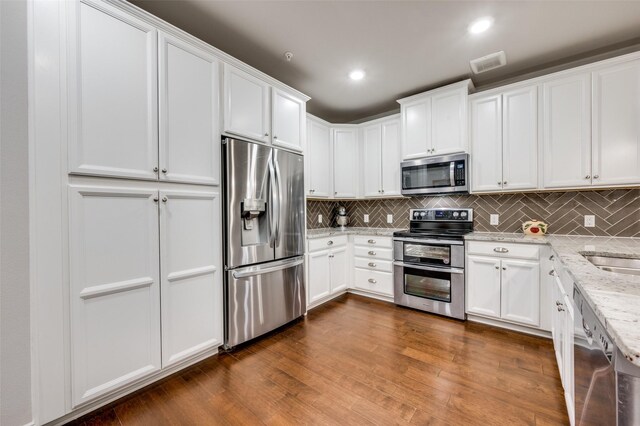 kitchen featuring white cabinets, backsplash, appliances with stainless steel finishes, and light stone countertops
