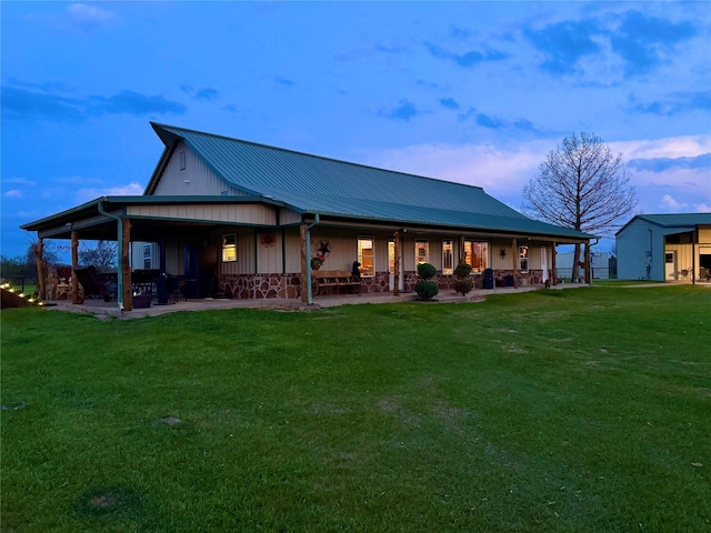back of house with stone siding, a yard, metal roof, and covered porch