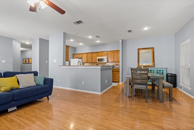 living area featuring light wood-style floors, visible vents, a ceiling fan, and baseboards