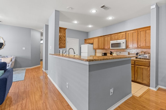 kitchen with light wood finished floors, dark stone countertops, visible vents, a sink, and white appliances